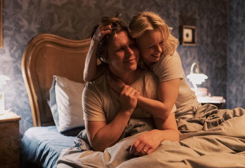 Kuvassa ovat Eero Milanoff ja Alma Pöysti vuoteessa. Milanoff istuu puolittain peiton alla ja Pöysti on hänen olkapäidensä yläpuolella ja pörröttää Milanoffin hiuksia.  