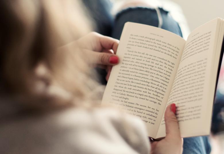 Kuvassa on nainen lukemassa kirjaa ja kuva on otettu takaapäin.