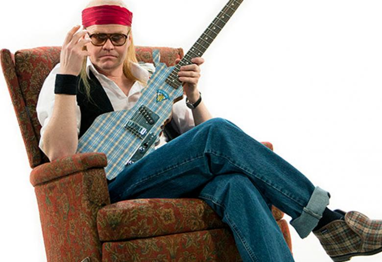 Kuvassa on Otto Kanerva Juicena istumassa ruskeassa nojatuolissa ja kitara kädessään.  Hänellä on punainen nauha päässään.