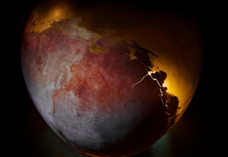 Kuvassa on tummalla pohjalla puolikas maapallo, jonka toiselta puolelta näkyy tulen välistä valoa.  