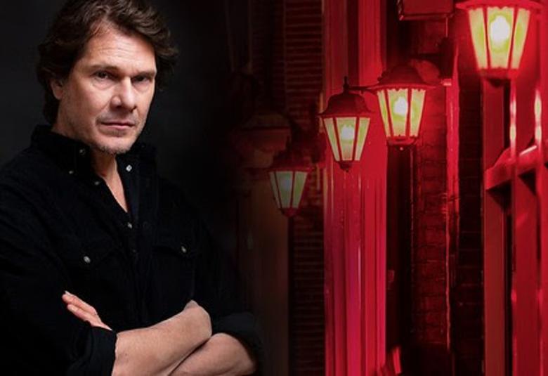 Kuvassa Kari Toivonen seisomassa tummalla taustalla ja oikealla on punaista seinää sekä kolme vanhanaikaista katulamppua.