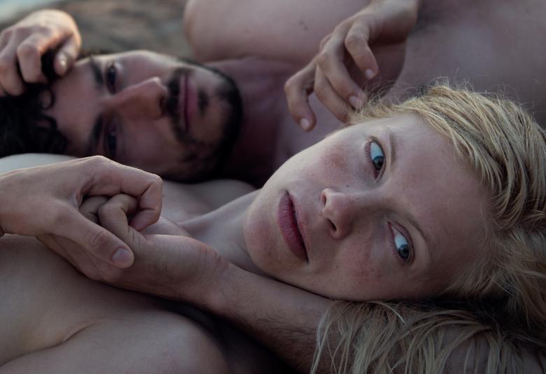 Kuvassa ovat Saara Kotkaniemi ja Nicola Perot lähikuvassa makaamassa ja he ovat vastakkaisissa suunnissa ilman vaatteita. Kuva on heidän yläosastaan.