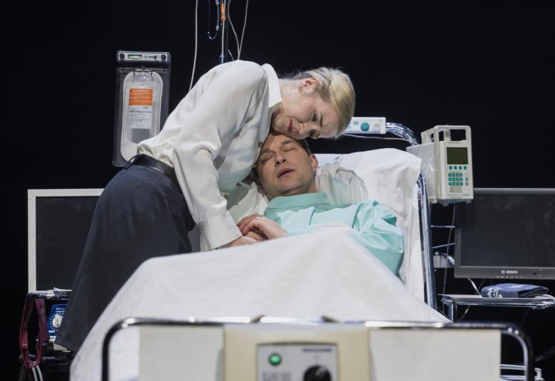 Kuvassa on Mikko Pörhölä sairaalasängyssä ja häntä lohduttaa Saana Hyvärinen.