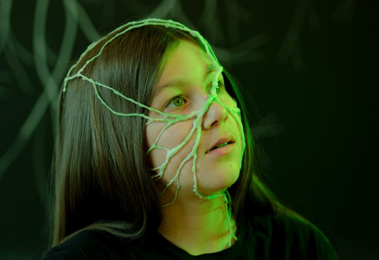 Kuvassa on noin kymmenvuotias tyttö kasvot ylöspäin ja hänellä on vihreitä rantuja pitkin kasvoja ja päätä.