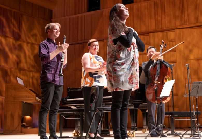Kuvassa on Outi Tarkiainen ja kolme soittajaa lavalla alaviistosta kuvattuna. Taustana on puun väriset seinät.