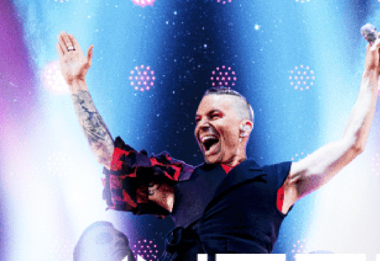 Kuvassa on Antti Tuisku puolivartalokuvassa kädet ylöspäin kohotettuna mustassa t-paidassa ja tausta on sininen.