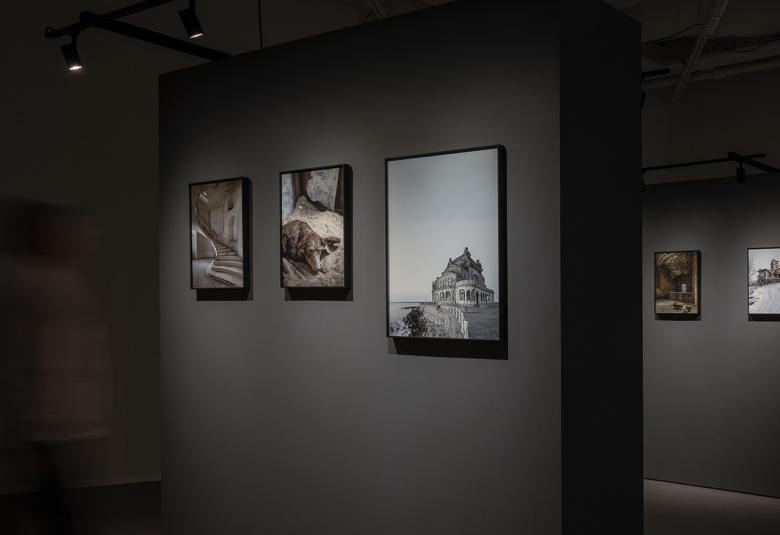 Kuvassa on Finnfoton näyttelytilaa, jossa on tumalla taustalla on seinälle ripustettuja valokuvia kehyksissä. 