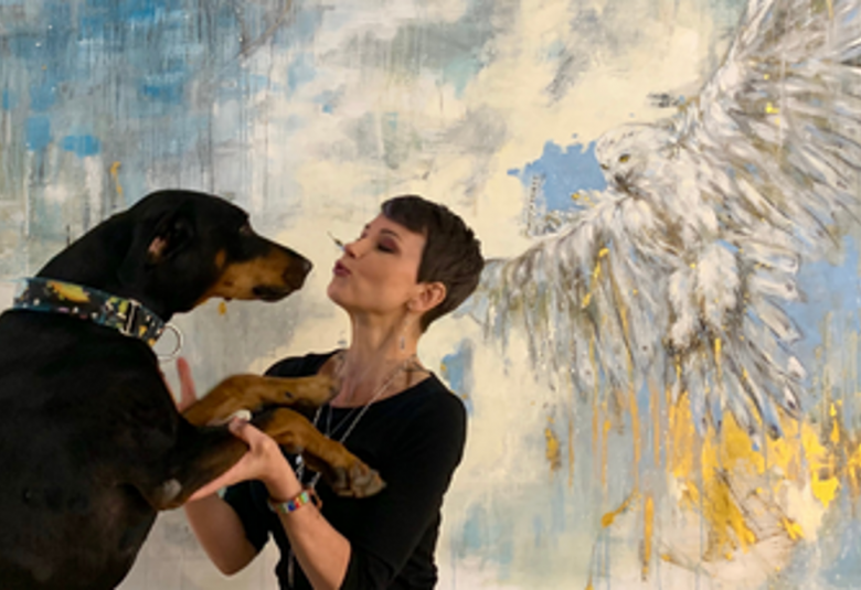 Kuvassa on Katariina Souri sivuttain ja vastakkain koiransa kanssa, jonka kuono on kohti hänen kasvojaan. Tausta on turkoosi.