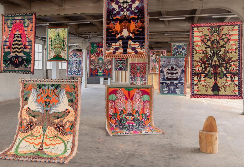 Kuvassa on ripustettuna useita erilaisia seinävaatteita näyttelytilassa.  