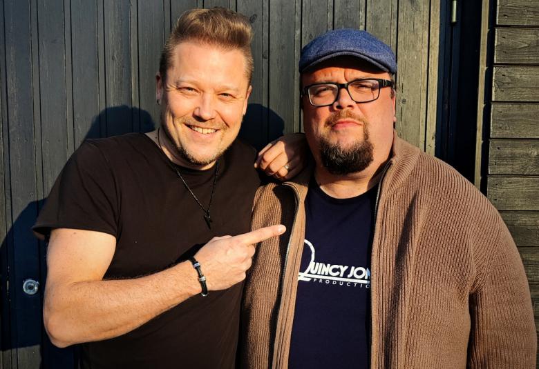 Kuvassa ovat Tomi Salesvuo  mustassa t-paidassa vasemmalla ja Sami Pitkämö pusakassa oikealla seisomassa ulkona.  Kuva on puolivartalokuva. 