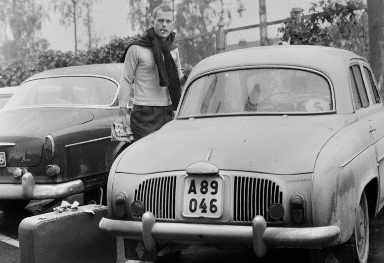 Kuvassa on Jörn Donner autonsa Renault Dauphinen vieressä ja kadulla on myös vieressä parkkeerattuna Volvo Amazon. Kuva on musta-valkoinen.