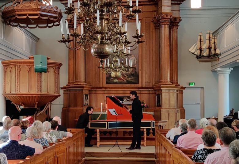 Kuvassa on Bence Boganyi soittamassa sivuttain fagottia alttarilla.  Taustalla on alttaritaulu ja suuri kristallikruunu sekä ruskeasta puusta veistetyt alttaritaulun kehykset ja alttari.  Keskellä on käytävä ja molemmin puolin yleisöä.