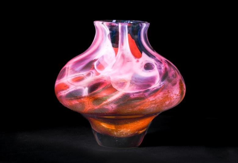 Kuvassa on mustalla pohjalla Uranuksen muotoinen lasiesine, joka on punertava.  Siitä lähtee keskeltä valkoisia liekkejä.