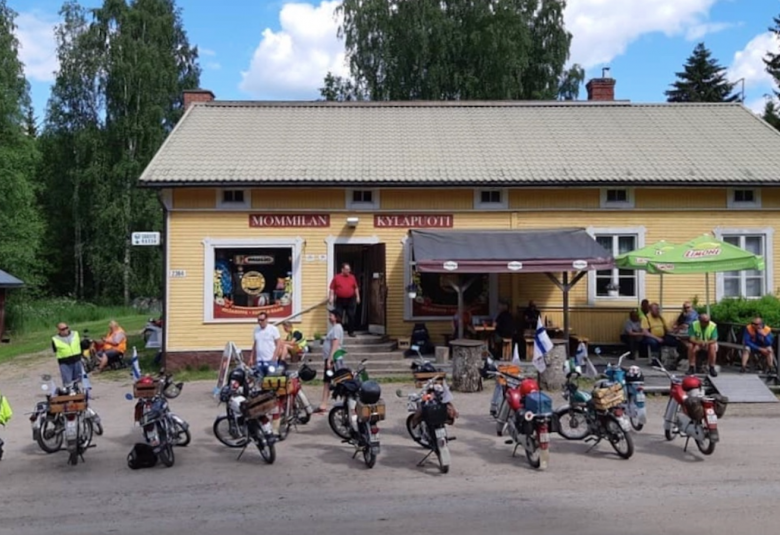 Kuvassa on Mommilan kyläpuodin keltainen rakennus, jonka edessä on mopoja.