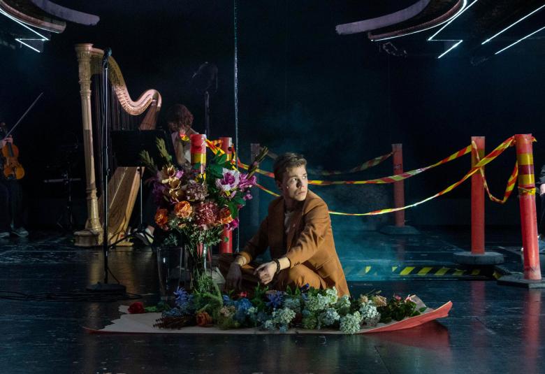 Kuvassa on mies pienessä kasvitarhassa puuhaamassa ja taustalla on harppu.  Sivussa on huomionauhaa ja niiden välillä punaiset tolpat. Oikealla pienellä näkyy vanhan miehen hahmo.