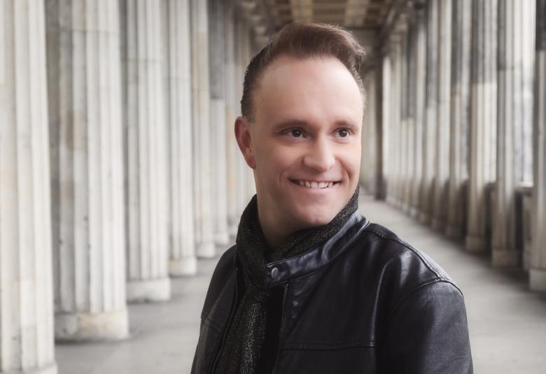 Kuvassa on Teijo Lindstöm puolivartalokuvassa ja mustassa nahkatakissa.  Taustalla on klassinen pylväikkö.