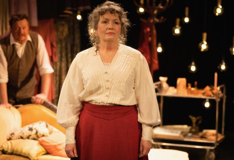 Kuvassa on Kristiina Hakovirta etualalla vaaleassa puserossa ja ruosteen punaisessa ppuolihameessa. Taustalla Mika Piispa sohvan takana.