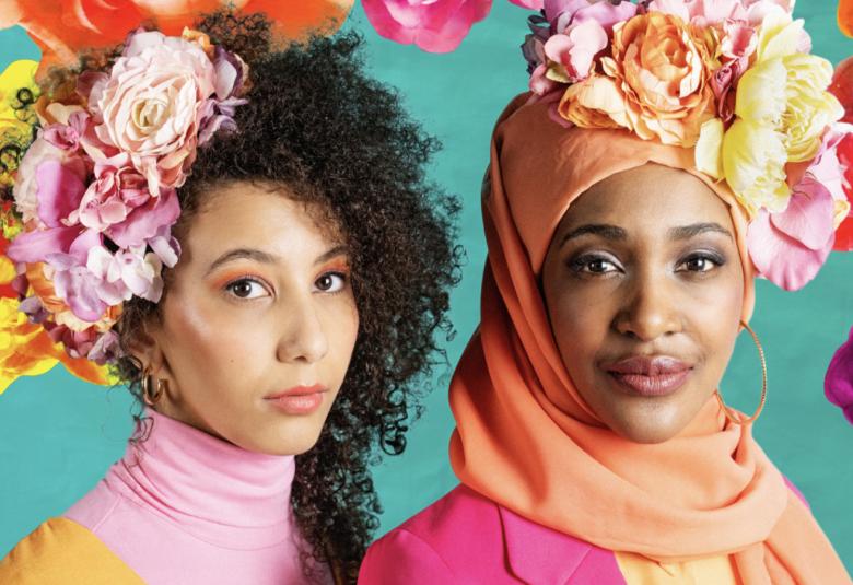 Kuvassa on kaksi nuorta naista. Vasemmalla olevalla naisella on tummissa hiuksissaan vaalean punaisia kukkia. Oikealla tummaihoisella naisella on päässään oranssi huivi ja vaaleita kukkia.  Taustalla on keltaisia ja oransseja kukkia turkoosilla pohjalla.