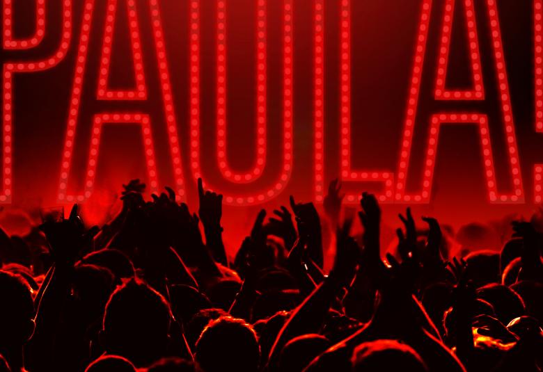 Kuvassa on punaisella pohjalla mustalla yleisöä, joka katsoo lavalle päinä.  Siellä lukee isoilla kirjaimilla Paula.