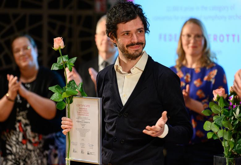 Kuvassa on voittaja Federico Perotti etualalla voittotaulu ja vaaleanpunainen ruusu kädessään.  Taustalla on kaksi naista, jotka ovat taustalla taputtaen käsiään.