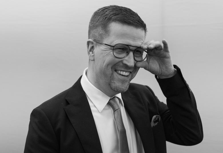 Kuvassa on Klaus Härö vinoittain ja vasemmalla kädellä hän kohottaa silmälasien sankaa. Hänellä on puvuntakki päällään ja valkoinen paita sekä kravatti. Kuva on musta-valkoinen.