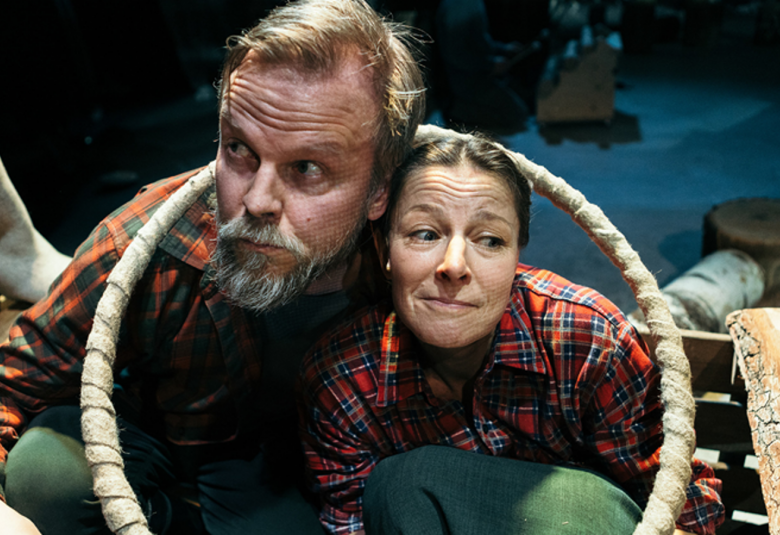 Kuvassa ovat naisnäyttelijä ja miesnäyttelijä lähikuvassa. Heillä on ruutupaidat päällään ja he istuvat vaalea rengas ympärillään.