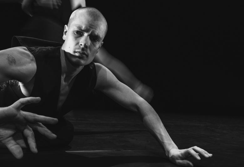 Kuvassa on miestannssija lalttialla kumartuneena eteenpäin nojaten vasempaan käteensä ja pitää oikeaa kättään koukussa. Kuva on musta-valkoinen.