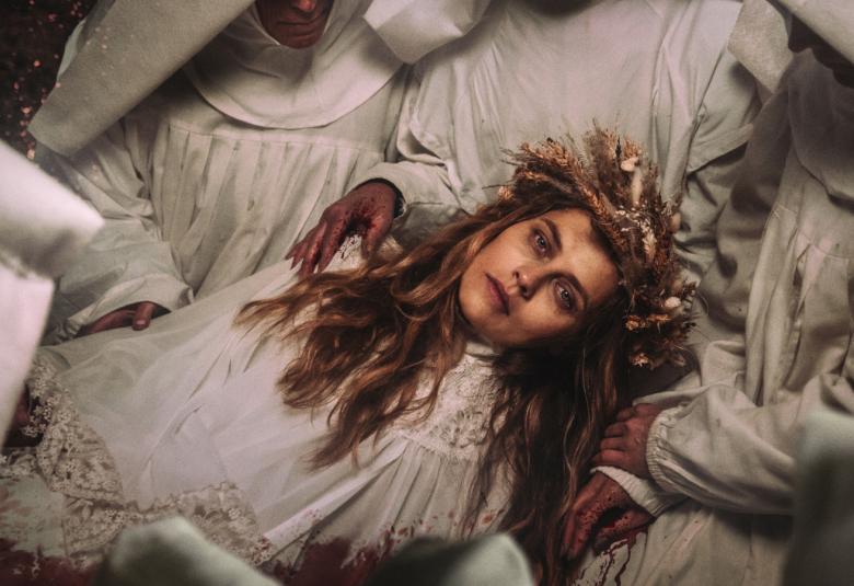 Kuvassa on Teresa Palmer makaamassa selällään vaaleat hiukset hajallaan ja vaaleassa röyhelöisessä mekossa.  Ylempänä on yksi vaaleassa nunnan kaavussa oleva henkilö ja ympärillä on vaaleaa lakanaa.