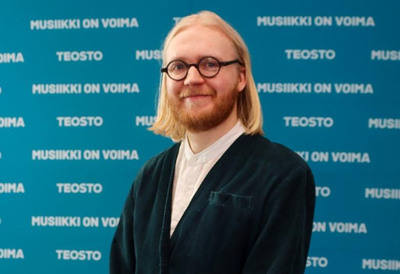 Kuvassa on Mikko Sarvanne seisomassa puolivartalokuvassa.  Hänellä on musta villatakki ja valkoinen paita päällään.  Tausta on sininen ja siinä on valkoisilla kirjaimilla toistuvasti sanat Teosto ja Musiikki on voima.