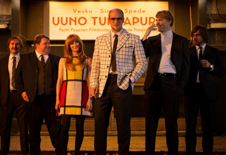 Kuvassa ovat Spede-elokuvan kuusi esiintyjää lavalla ja taustalla on kyltti, jossa lukee Uuno Turhapuro ja Vesku, Simo ja Spede. 