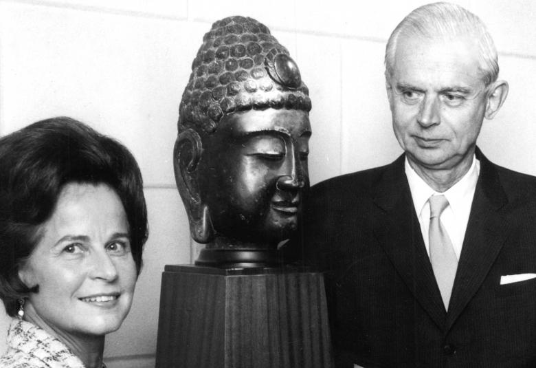 Kuvassa ovat Marie-Louise ja Gunnar Didrichsen buddhan päätä esittävän patsaan vierellä. Kuva on musta-valkoinen.