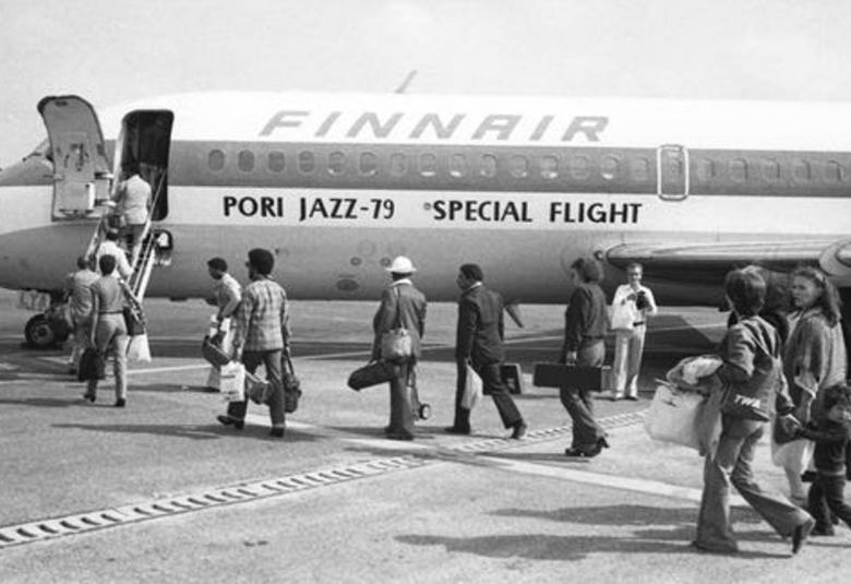 Kuvassa on Finnairin kone, johon on menossa rivissä matkustajia. Koneessa lukee Poro Jazz -79, Special Flight.  Kuva on musta-valkoinen.