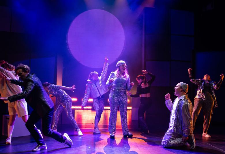 Kuvassa on valaistu näyttämö ja siinä nuoria esiintyjiä.  Kuvan sävy on sinisävyinen.