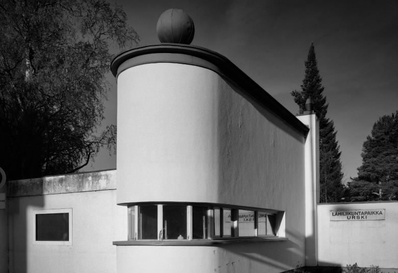 Kuvassa on edestäpäin kuvattuna kioski, joka levenee taaksepäin ja etupää on pyöristetyn muotoinen.