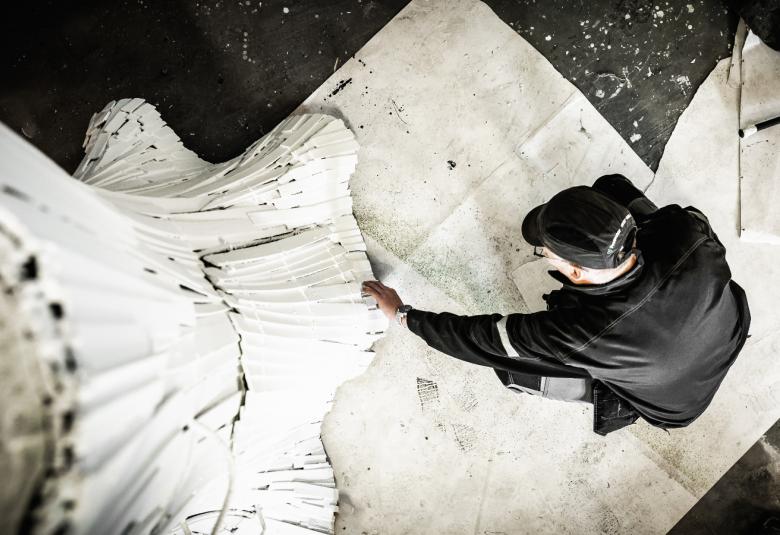 Kuvassa on mustapukuinen lavastaja kuvattuna ylhäältä päin.  Vasemmalla on vaalea, klassinen pylväs. Lattia on musta.