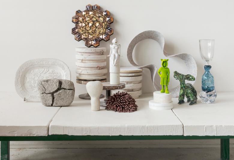 Kuvassa on valkealla kivipöydällä erilaisia valkoisia keramiikkaesineitä ja ylimpänä on ruskea kukkamainen esine.