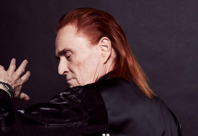 Kuvassa on Tommi Läntinen selin ja hänestä näkyy ylhäällä oleva käsi. Kuva on puolivartalokuva.