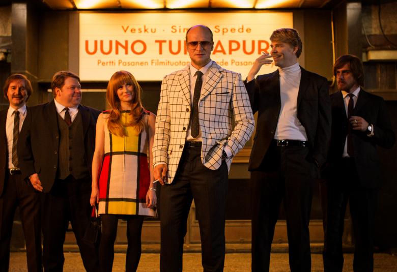 Kuvassa ovat elokuvan kuusi päähenkilöä rivissä Risto Niemisen takana ja heillä on pikkutakit päällä. Vasemmalla keskellä Niemisen vieressä on Minka Kuustonen, jolla on isoruutuinen minihame.  Ruudut ovat kirkkaan värisiä ja eri väreissä. Ylhäällä on kyltti Uuno Turhapuro.