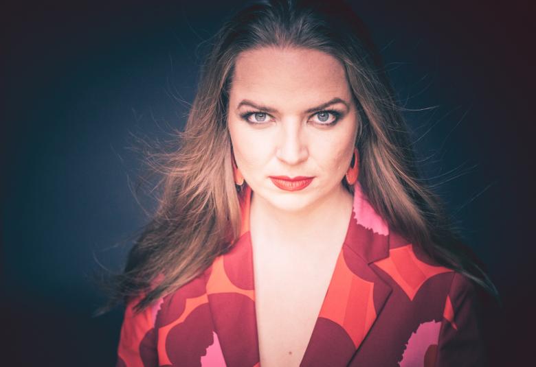 Kuvassa on Cecilia Damström puolivartalokuvassa. Hänellä on v-aukkoinen puku, joka punainen Marimekon Unikko-kuosinen.