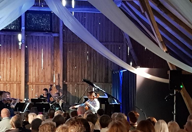 Kuvassa ovat Kaakon Kamarimusiikin soittajat Jukka Merjanen, Ville Koponen, Maria Krykov ja Tuomas Ylinen sekä Tuomas Turriago taustallaan ladon seinää ja ylhäällä on valkoista nauhaa vedettynä vinosti alaspäin.  Edessä on yleisöä.