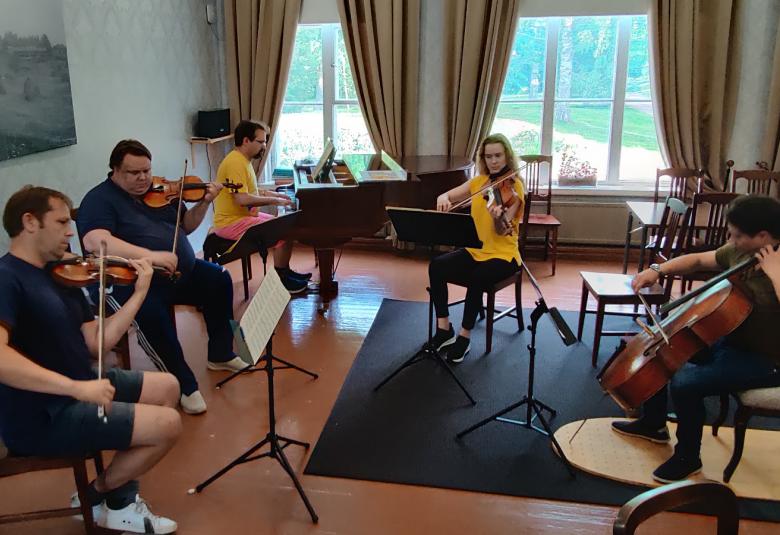 Kuvassa ovat Jukka Merjanen, Ville Koponen, Tuomas Turriago, Kirsikka de Leval Jezierski ja Samuli Peltonen soittamassa puolikaaressa vanhoilla huonekaluilla sisustetussa huoneessa.