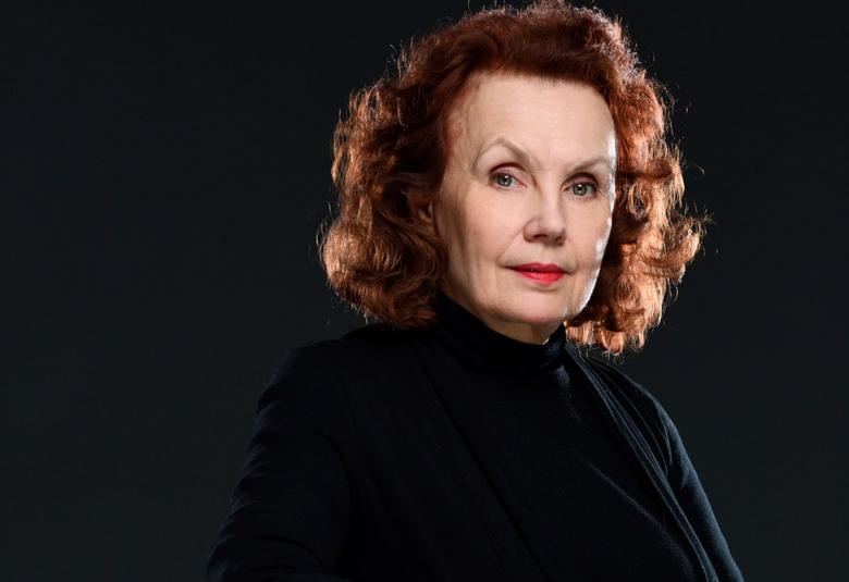 Kuvassa on Kaija Saariaho puolivartalokuvassa, jossa näkyy hänen kasvonsa.  Tausta on musta ja hänellä on musta pusero päällään.