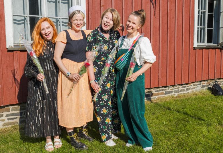 Kuvassa ovat Enkel-yhtyeen nuoret naiset Maija Pokela (vas.) Leija Lautamaja, Miia Palomäki ja Iida Savolainen ja heillä on joko pitkät puvut tai Savolaisella vihreät farkkuhaalarit. Taustalla on puna-valkoinen talo..