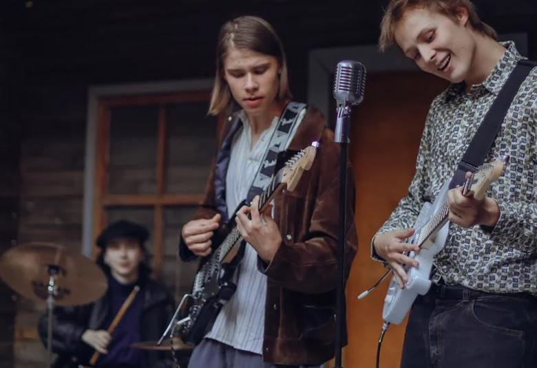 Kuvassa on kaksi nuorta, teini-ikäistä poikaa soittamassa kitaraa.  Taustalla näkyy hieman yleisöä.