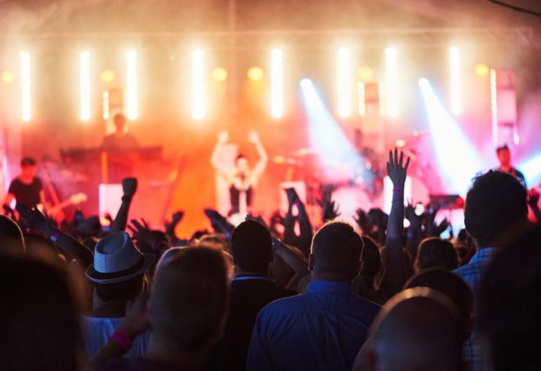 Kuvassa on esiintyjiä lavalla ja yllä on keltaista valoa. Edessä on yleisöä.