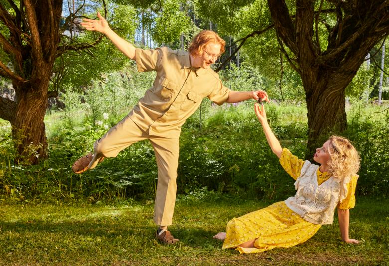 Kuvassa ovat Ylermi Rajamaa tanssimassa keltaisessa puvussa ja Minka Kuustonen istumassa nurmikolla.  Hänellä on myös keltainen puku. Taustalla on kahden puun rungot ja kohtaus on puistossa.