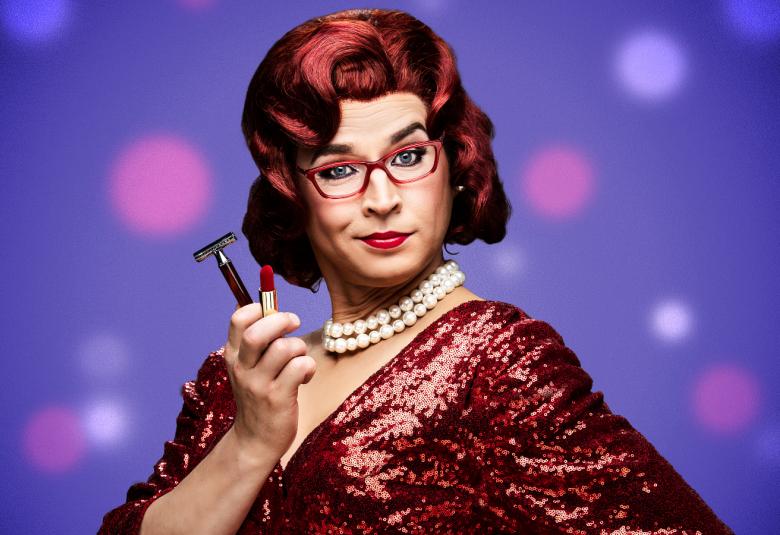 Kuvassa on Antti Lang, joka on pukeutunut naiseksi ja josta on puolivartalokuva.  Hänellä on punaiset hiukset ja hän näyttää kädessään olevaa huulipunaa ja partahöylä. Kaulassa on valkoiset helmet ja kuvassa näkyy purpuran punaista pukua.