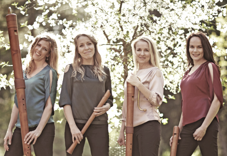 Kuvassa ovat Bravaden neljä naisjäsentä seisomassa nokkahuilujensa kanssa. Heillä on harmaat ja ruskehtavat t-paidat päällään. Taustalla on vihreitä lehtipuita ja vaaleaa lehvistöä, johon osuu valoa.