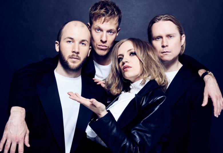 Kuvassa ovat Haloo Helsingin neljä jäsentä puolivartalokuvassa.  Heillä on mustat jakut ja valkoiset paidat. Edessä Ellillä vasemman käden kämmen ylöspäin.