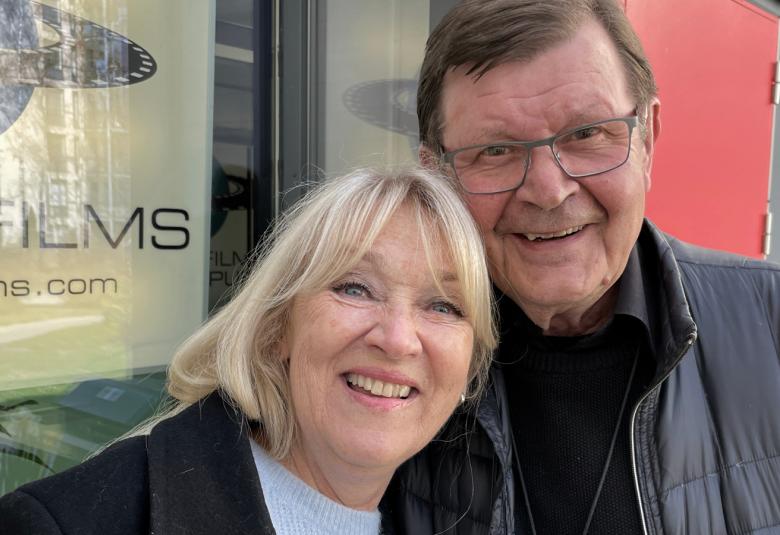 Kuvassa ovat Jaana Saarinen ja Heikki Kinnunen ulkona. Saarisella on musta takki ja vaalean sininen pusero. Heikki Kinnusella on musta nahkatakki.  Taustalla on seinää ja vasemmalla filmijuliste.